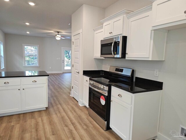 kitchen with dark countertops, light wood-style flooring, appliances with stainless steel finishes, open floor plan, and white cabinetry