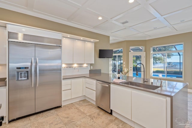 kitchen with kitchen peninsula, stainless steel appliances, white cabinets, coffered ceiling, and sink