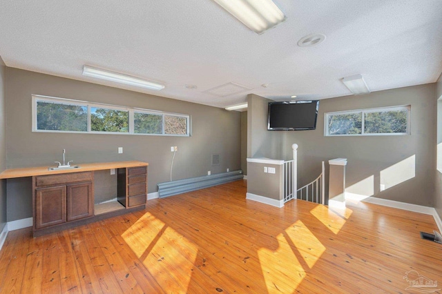 unfurnished office featuring sink, a baseboard radiator, a textured ceiling, and light hardwood / wood-style flooring