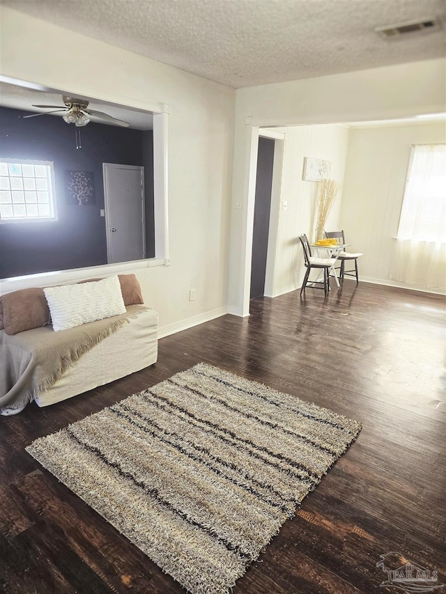 living room with ceiling fan, a textured ceiling, and dark hardwood / wood-style flooring