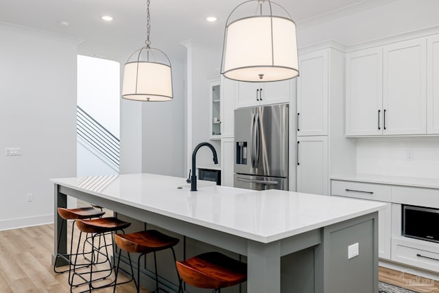 kitchen featuring an island with sink, stainless steel refrigerator with ice dispenser, and ornamental molding