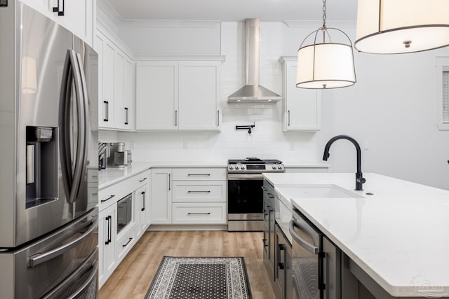 kitchen featuring white cabinets, wall chimney exhaust hood, decorative light fixtures, and appliances with stainless steel finishes