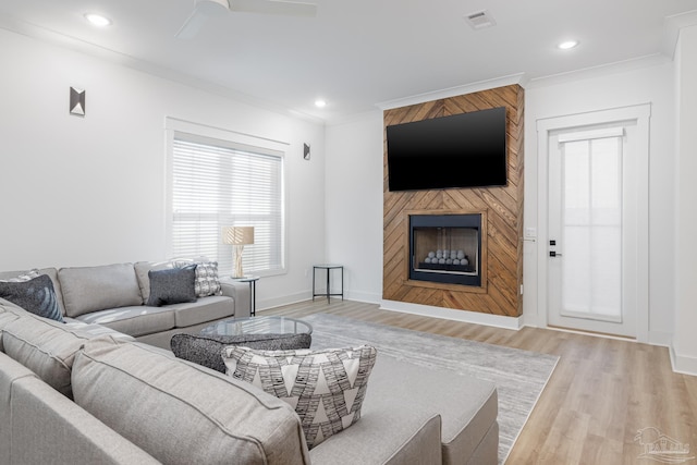 living room with ceiling fan, crown molding, a fireplace, and light hardwood / wood-style flooring