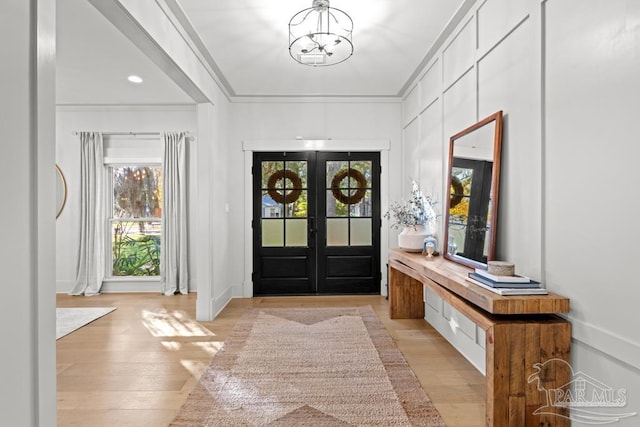 foyer entrance featuring a notable chandelier, light hardwood / wood-style floors, ornamental molding, and french doors