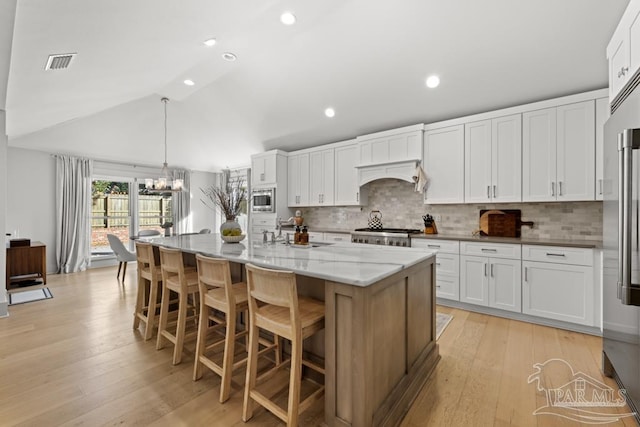 kitchen featuring built in appliances, a center island with sink, white cabinets, and lofted ceiling