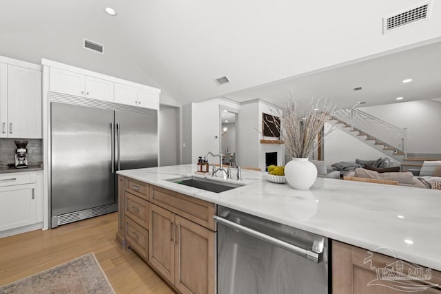 kitchen featuring lofted ceiling, white cabinets, sink, light wood-type flooring, and appliances with stainless steel finishes