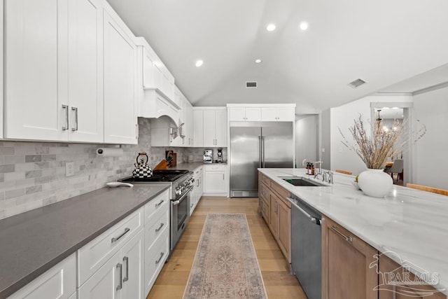 kitchen featuring high quality appliances, decorative backsplash, light stone countertops, a notable chandelier, and white cabinetry