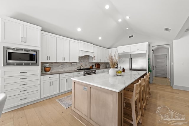 kitchen with a center island, lofted ceiling, white cabinets, built in appliances, and tasteful backsplash