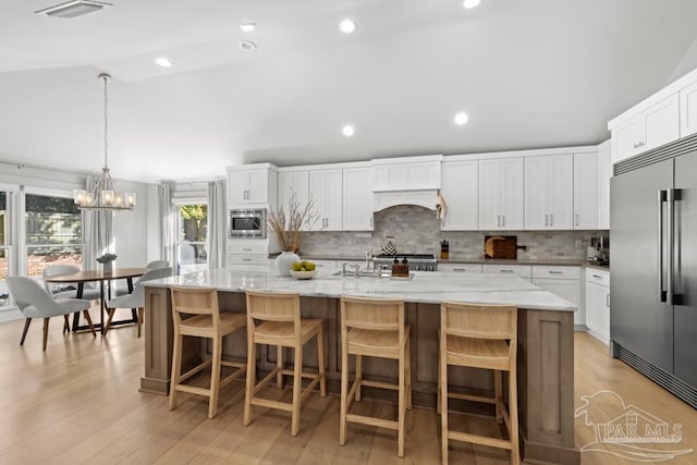 kitchen with built in appliances, a spacious island, and white cabinets