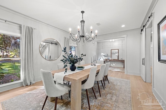 dining room featuring a barn door, light hardwood / wood-style floors, an inviting chandelier, and crown molding