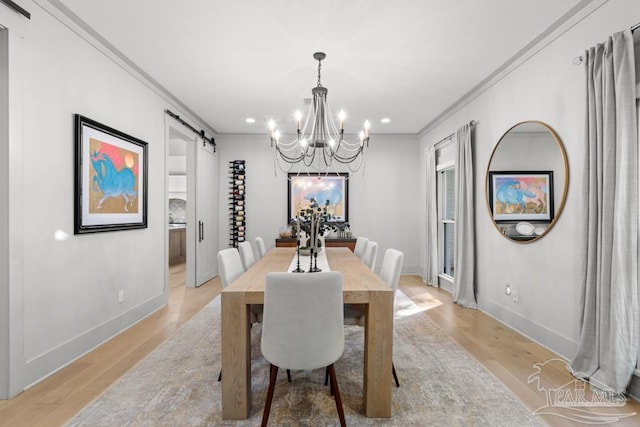 dining area with a barn door, light wood-type flooring, a notable chandelier, and ornamental molding