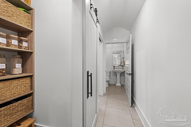 corridor featuring light tile patterned floors, a barn door, lofted ceiling, and sink