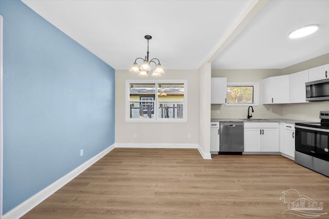 kitchen with white cabinetry, stainless steel appliances, decorative light fixtures, and sink