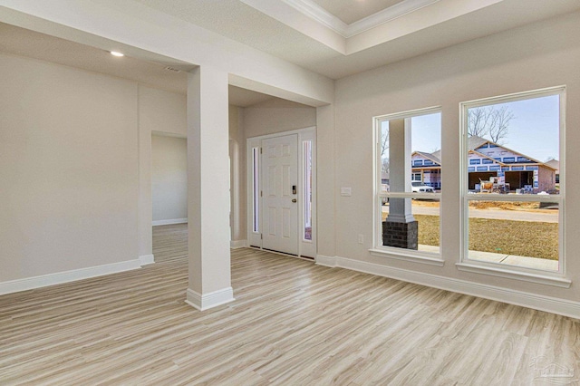 entrance foyer with ornamental molding, a raised ceiling, and light wood-type flooring