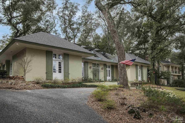 ranch-style house featuring roof with shingles and stucco siding