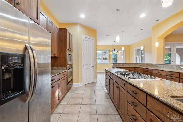 kitchen with light tile patterned floors, stainless steel appliances, pendant lighting, light stone counters, and an inviting chandelier