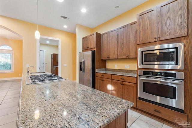 kitchen featuring stainless steel appliances, light stone countertops, a center island, pendant lighting, and light tile patterned flooring