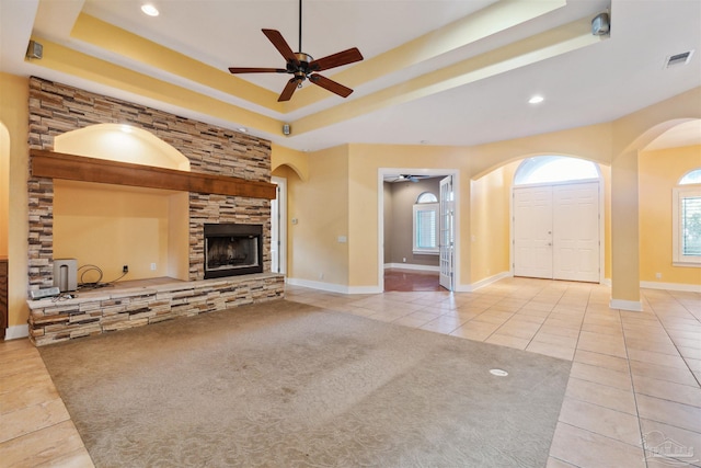 unfurnished living room with ceiling fan, a raised ceiling, light tile patterned floors, and a fireplace