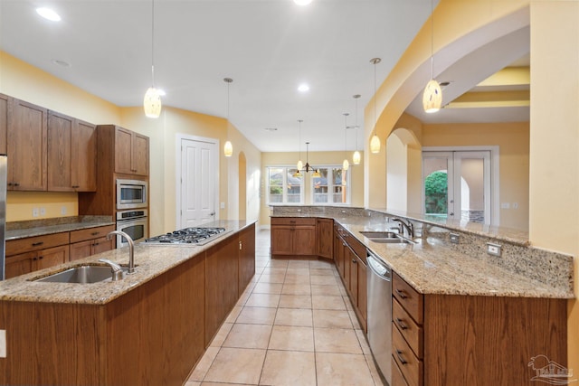 kitchen featuring appliances with stainless steel finishes, light stone countertops, decorative light fixtures, and sink