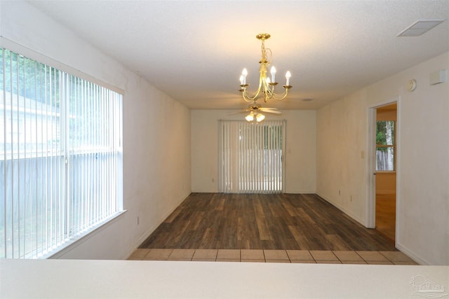 spare room featuring a healthy amount of sunlight, ceiling fan with notable chandelier, and dark hardwood / wood-style flooring