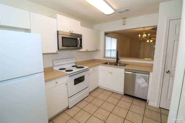 kitchen with an inviting chandelier, light tile patterned floors, stainless steel appliances, sink, and white cabinetry