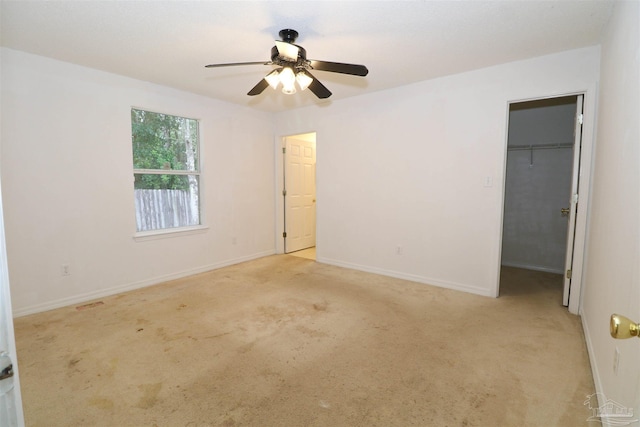 unfurnished bedroom with a walk in closet, ceiling fan, light colored carpet, and a closet