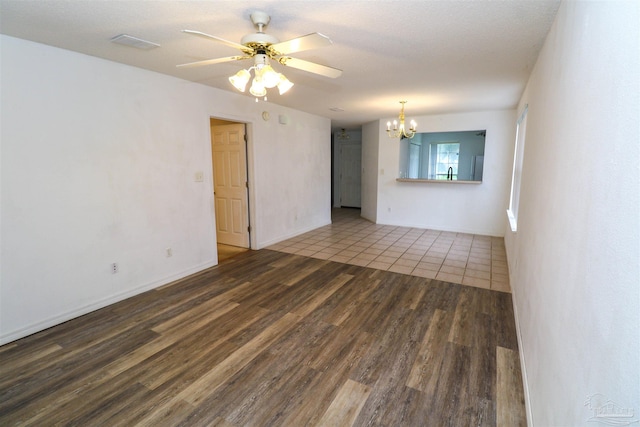 spare room featuring dark wood-type flooring, ceiling fan with notable chandelier, and a textured ceiling