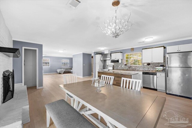 931 Pocahontas Dr, Ft Walton Beach, FL 32547 - dining room featuring an inviting chandelier, crown molding, light hardwood / wood-style flooring, and a brick fireplace