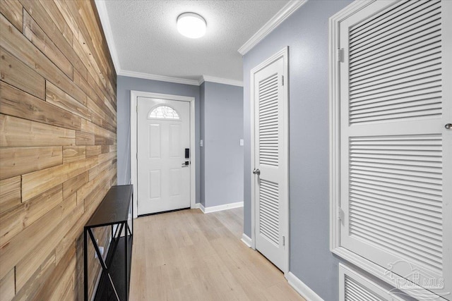 interior space with a textured ceiling, crown molding, wood walls, and light wood-type flooring