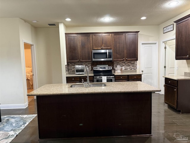 kitchen with stainless steel appliances, light countertops, a sink, and an island with sink