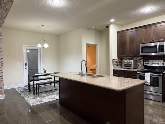 kitchen featuring decorative light fixtures, stainless steel appliances, a sink, dark brown cabinets, and a center island with sink