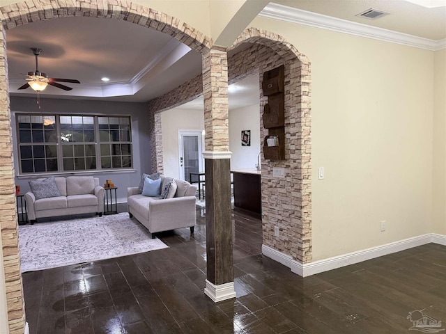 living area featuring arched walkways, dark wood-style flooring, visible vents, decorative columns, and crown molding