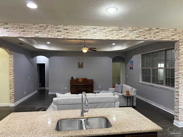 kitchen featuring arched walkways, a raised ceiling, and a sink