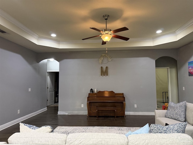 living area with baseboards, arched walkways, dark wood-type flooring, and a tray ceiling