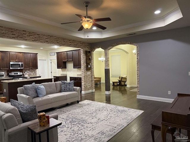 living room featuring arched walkways, dark wood-type flooring, visible vents, ornamental molding, and a raised ceiling