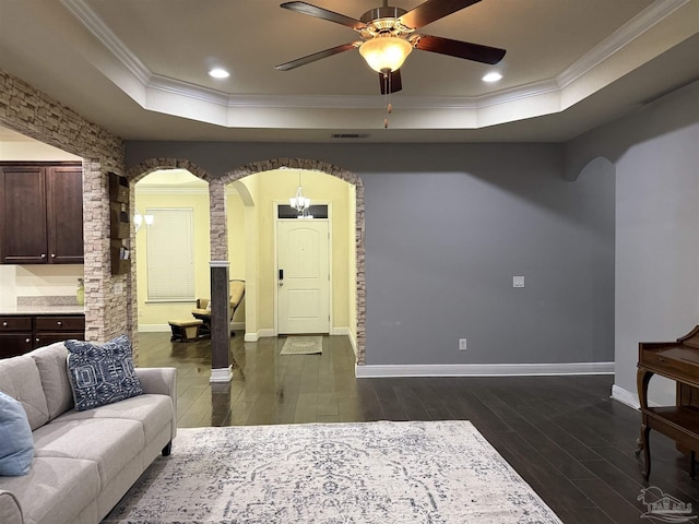 living room with dark wood-style floors, a tray ceiling, arched walkways, crown molding, and baseboards