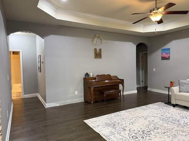 living area featuring arched walkways, dark wood-style flooring, baseboards, a raised ceiling, and crown molding