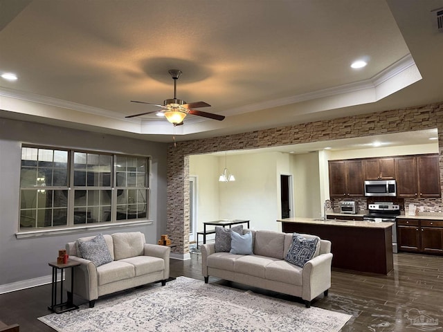 living room with ceiling fan, dark wood-style flooring, baseboards, a tray ceiling, and crown molding