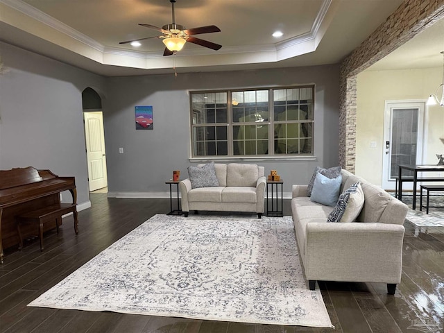 living area with a tray ceiling, dark wood-style flooring, crown molding, and arched walkways