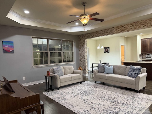 living area featuring a tray ceiling, recessed lighting, ornamental molding, dark wood-type flooring, and baseboards