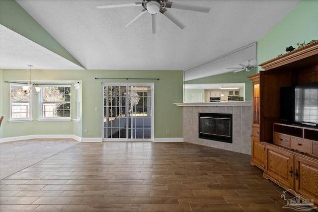 unfurnished living room featuring vaulted ceiling, ceiling fan with notable chandelier, a textured ceiling, and a fireplace