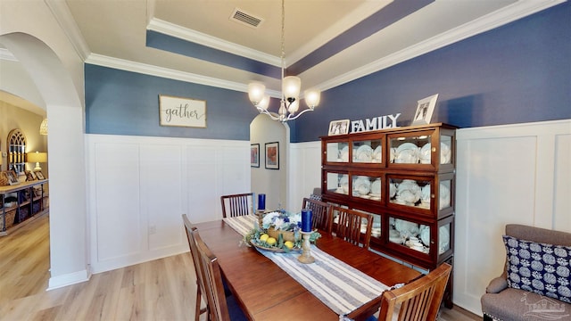 dining space featuring light wood-type flooring, a raised ceiling, crown molding, and a notable chandelier