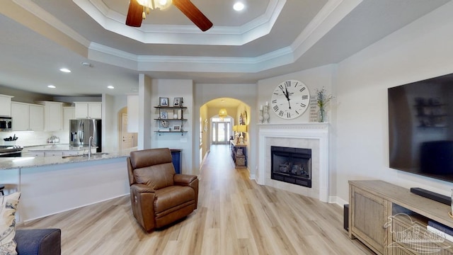 living room featuring light hardwood / wood-style floors, a raised ceiling, crown molding, and a tile fireplace