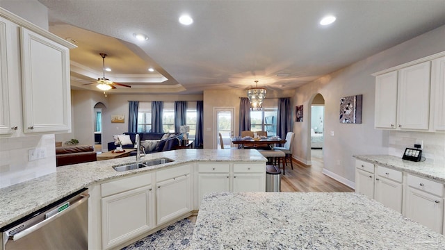 kitchen with stainless steel dishwasher, sink, a tray ceiling, and tasteful backsplash