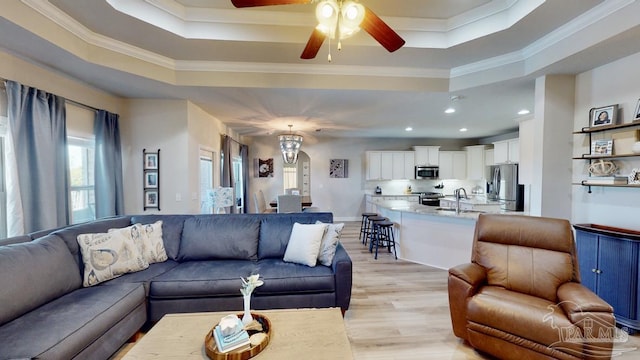 living room featuring ceiling fan, sink, a raised ceiling, light hardwood / wood-style flooring, and ornamental molding