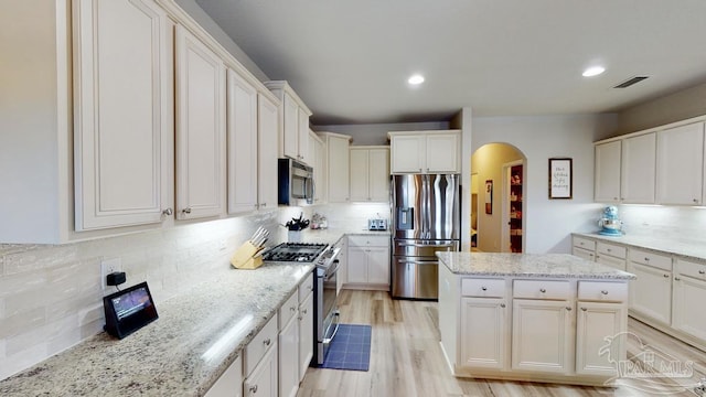 kitchen with light hardwood / wood-style flooring, decorative backsplash, appliances with stainless steel finishes, light stone counters, and white cabinetry