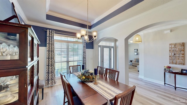 dining area featuring a tray ceiling, light hardwood / wood-style flooring, ornamental molding, and a notable chandelier