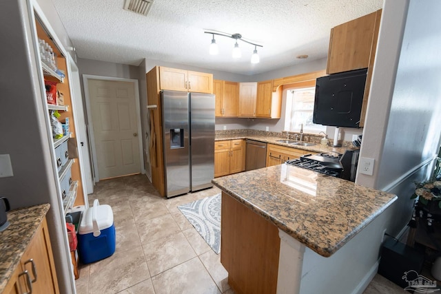 kitchen featuring a peninsula, dark stone counters, stainless steel appliances, and a sink