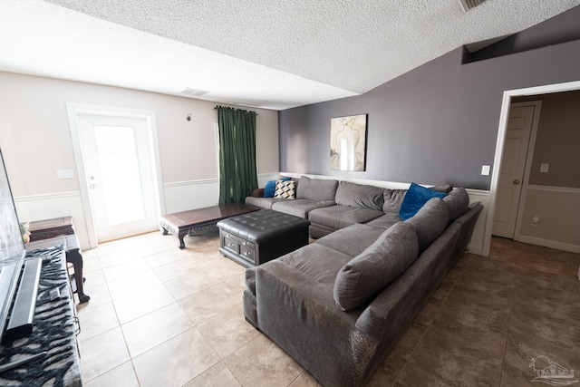 living area featuring light tile patterned floors, visible vents, a textured ceiling, and wainscoting