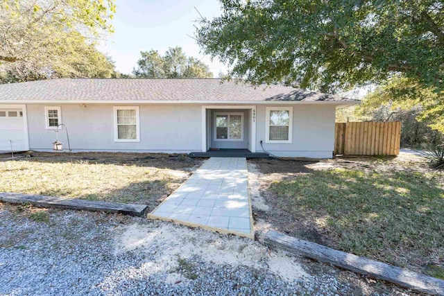 single story home featuring an attached garage, a shingled roof, fence, and stucco siding